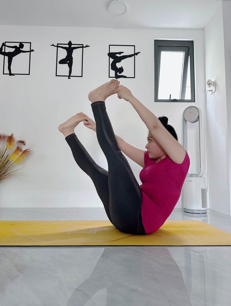 Tư thế con thuyền nắm chân trên thảm vàng tại phòng tập yoga Cần Thơ